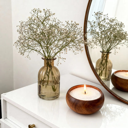 Vase with baby's breath flowers and wooden candle holder on a white surface.