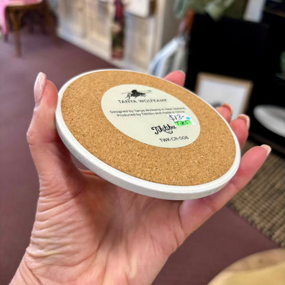 Cork coaster with a label held in a hand, blurred indoor background