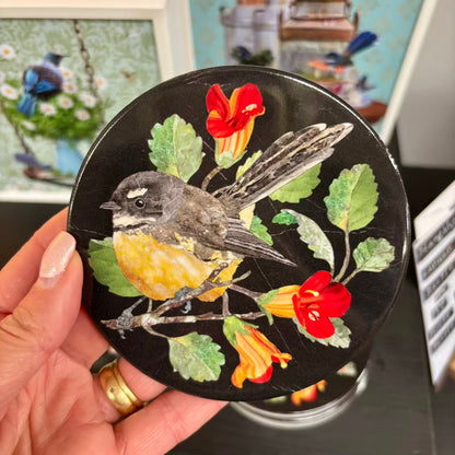 Round compact mirror with a bird and floral design held by a hand.
