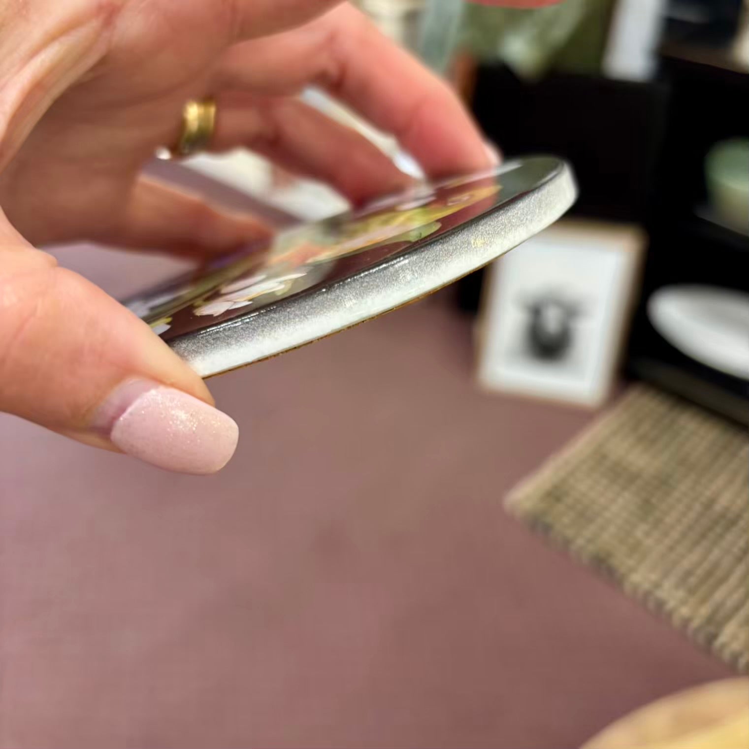 Hand holding a ceramic coaster with a blurred background