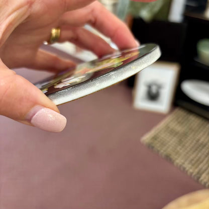 Hand holding a ceramic coaster with a blurred background