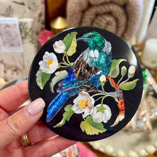 Decorative coaster with a colourful bird and floral design held by a hand.