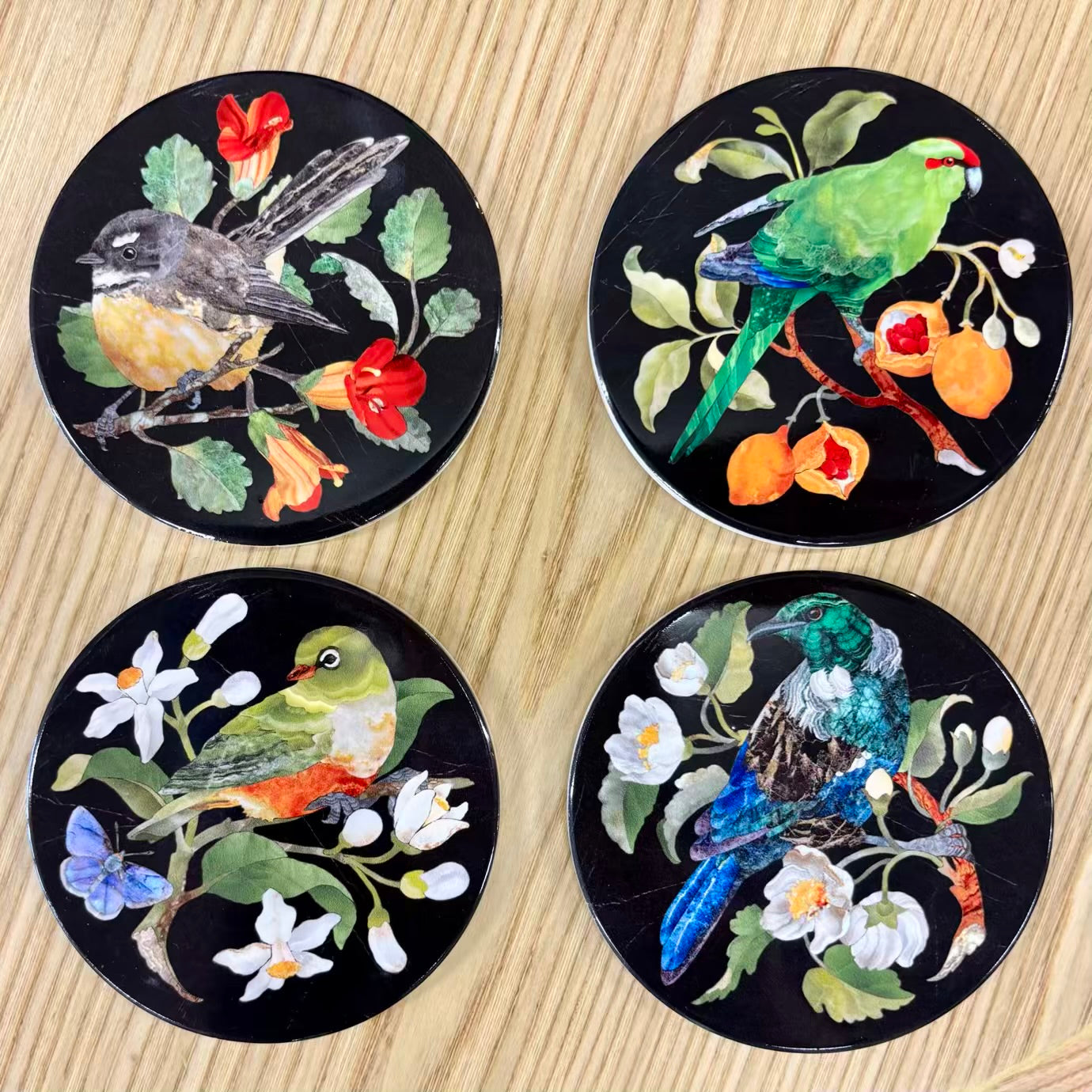 Four decorative coasters with bird and floral designs on a wooden surface
