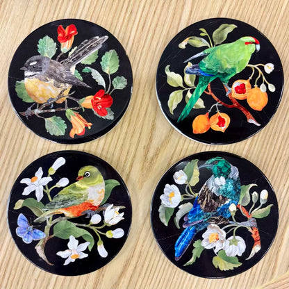 Four decorative coasters with bird and floral designs on a wooden surface