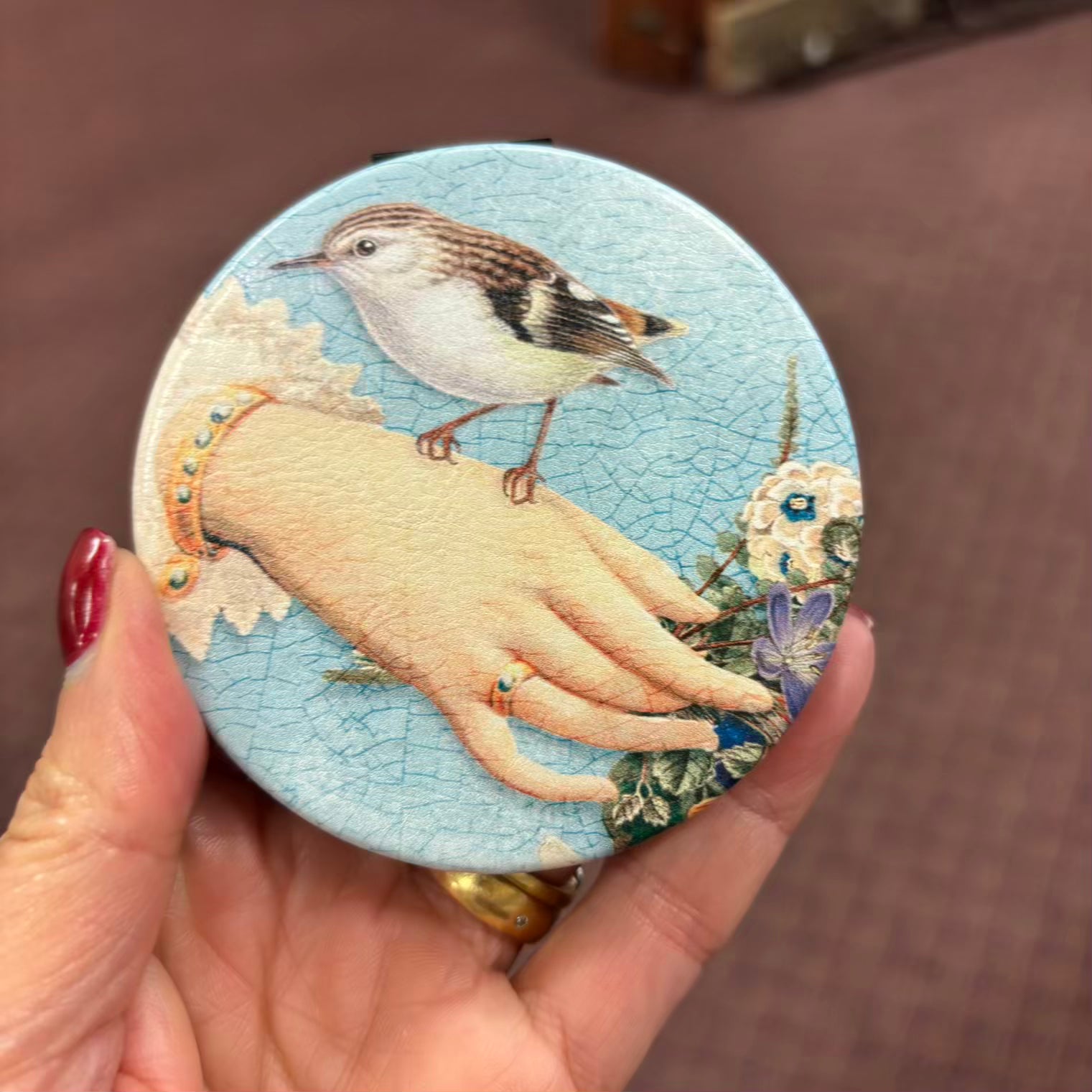 Round decorative item with a hand and bird design held by a hand.