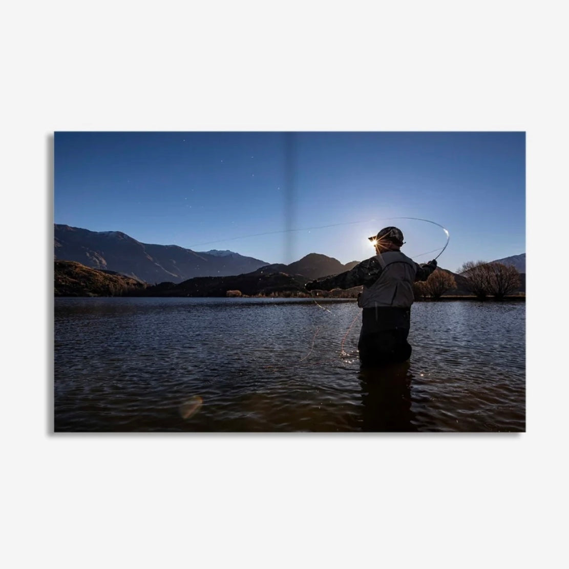 Person fly fishing in a lake with mountains in the background