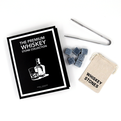 A whiskey stone collection gift set on a white background, including a black and white branded booklet, gray stone cubes, metal tongs, and a beige drawstring pouch labeled 'Whiskey Stones'.