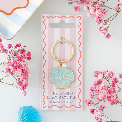 Enamel keyring with shell design on a pink and white striped card surrounded by pink flowers.