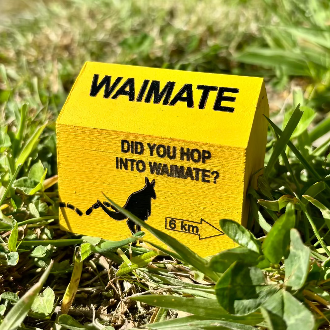 Yellow sign with text 'WAIMATE DID YOU HOP INTO WAIMATE?' on grass