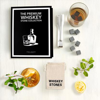 Whiskey stones with a glass of whiskey, lemon, and herbs on a white surface.