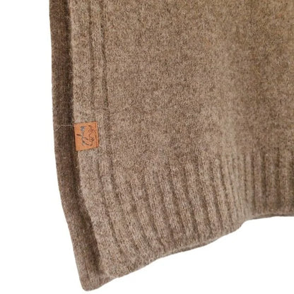 Close-up of a ribbed knit sweater in a warm taupe-brown color, showing a small tan brand tag sewn onto the sleeve.