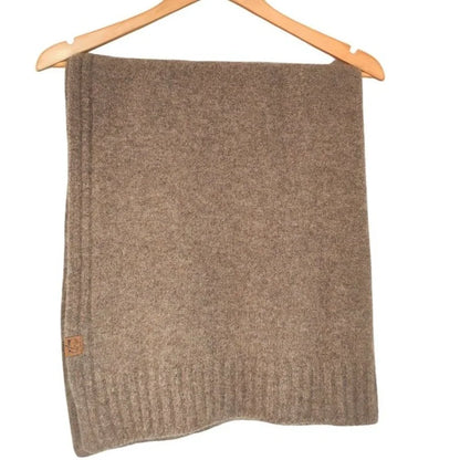 A brown knit blanket or throw hanging from a wooden hanger against a plain white background.
