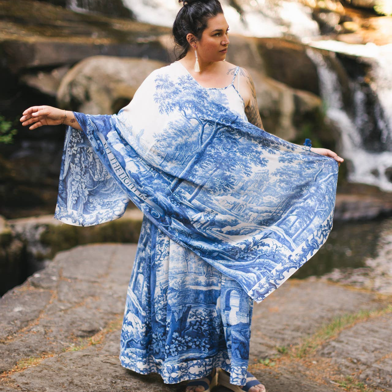 Woman in a blue patterned dress standing by a waterfall