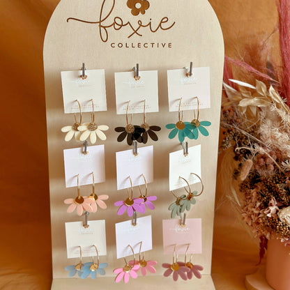 Earring display stand with 'foxiie collective' branding on a warm brown background