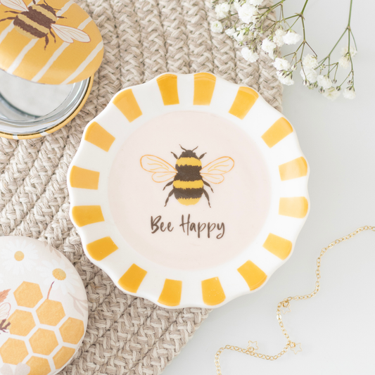 A round ceramic dish with a scalloped rim, featuring a yellow and black bumblebee illustration and the words 'Bee Happy' in brown script. The dish has alternating yellow and white stripes around the rim.