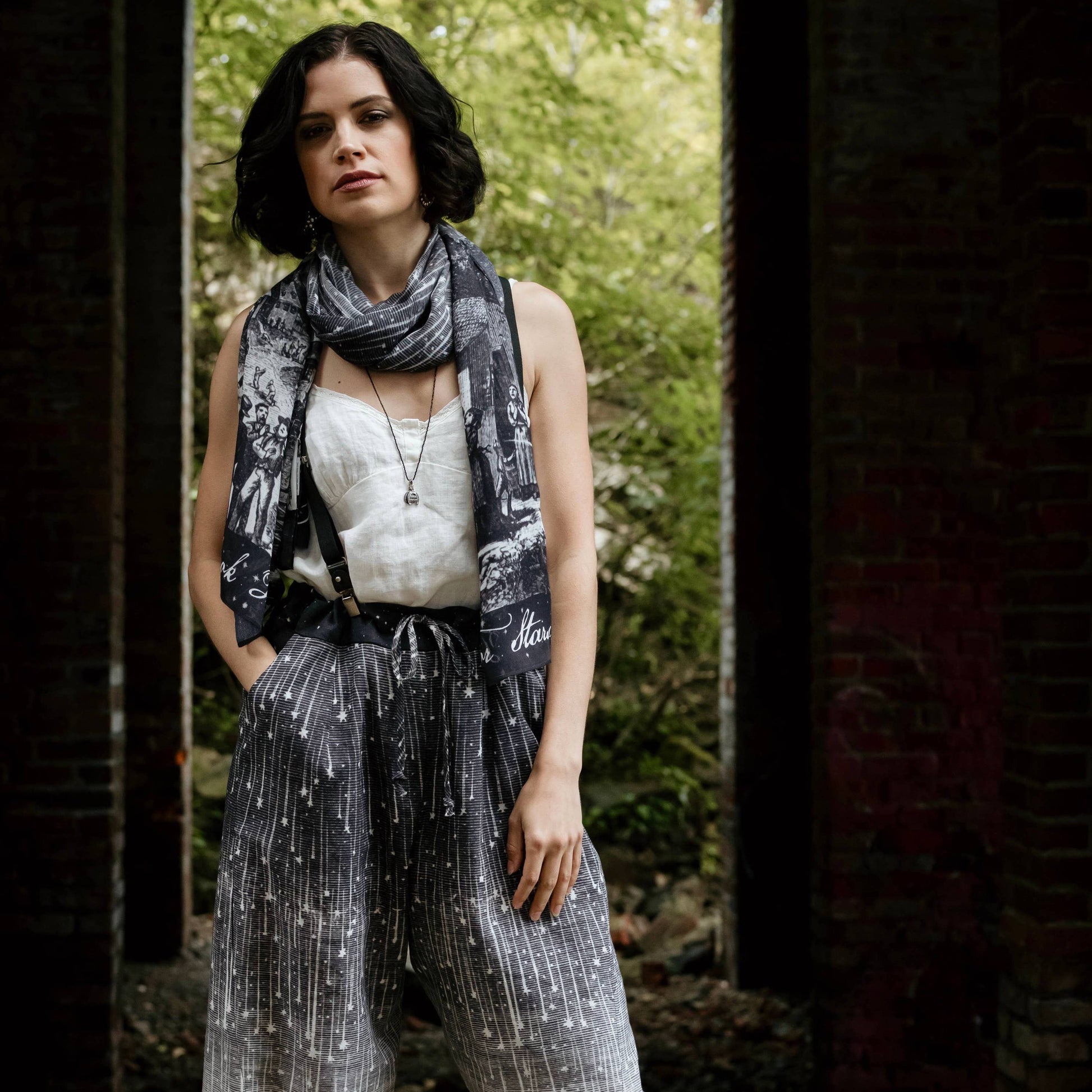 Woman wearing a patterned scarf and pants standing in a natural setting.