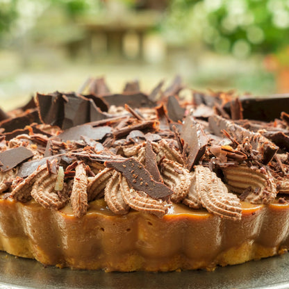Chocolate-topped tart on a metal stand with a blurred garden background