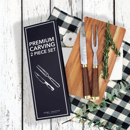 Premium carving 2-piece set by Home Chapter, including a carving knife and carving fork, shown with their black presentation box on a rustic white wood background with a black-and-white checkered cloth, wooden cutting board, and greenery.