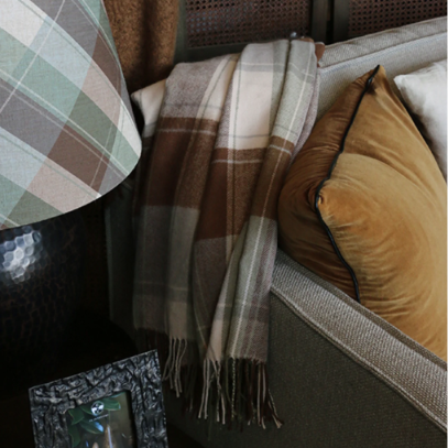 Plaid blanket draped over a sofa with a lamp and book in the foreground