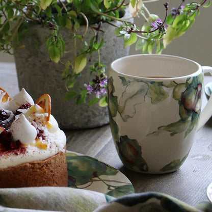 Cup with floral design, small cake, and plant on a table