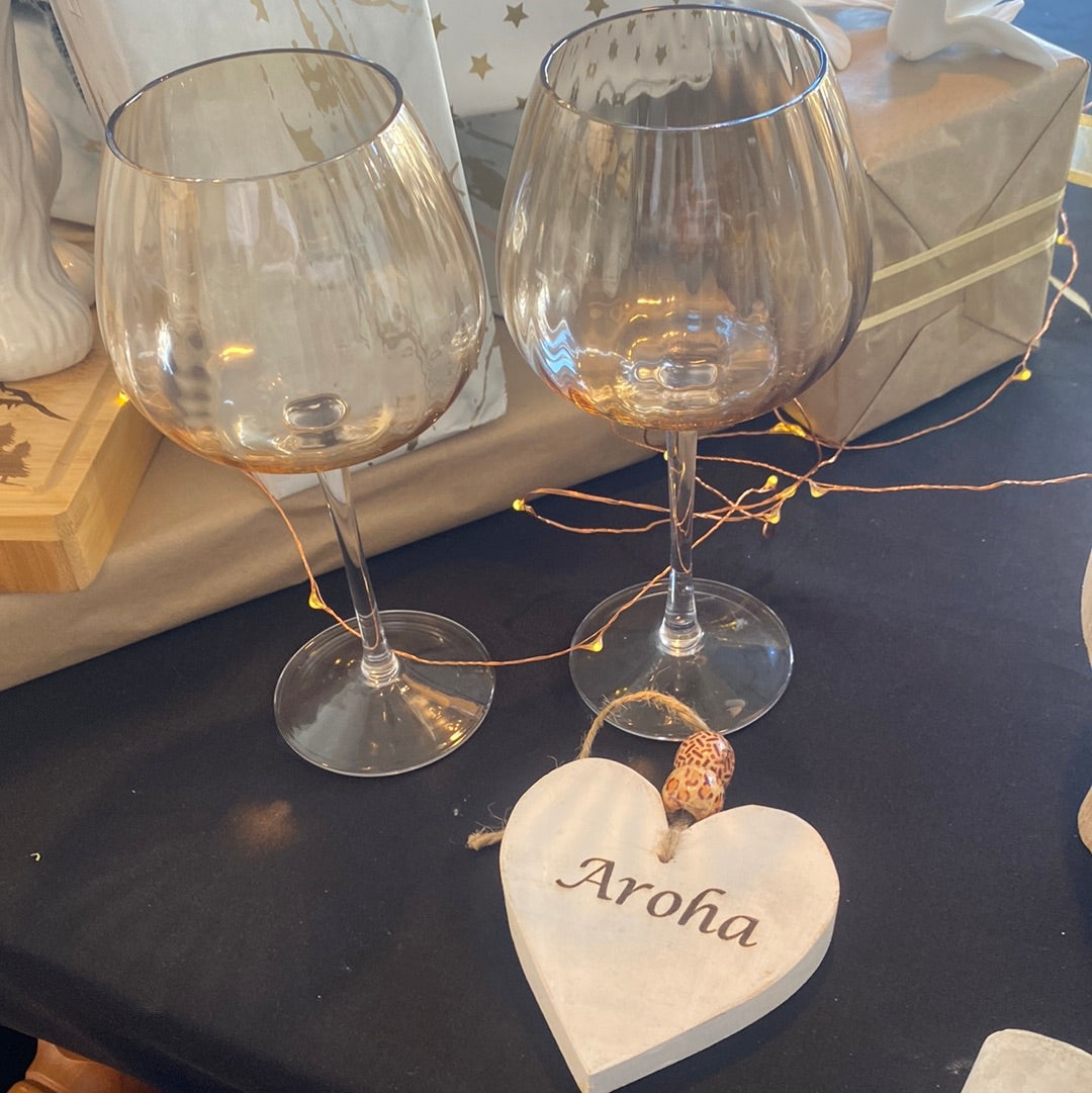 Two wine glasses with a ribbed design and amber hue, sitting on a table with a small white heart-shaped plaque that reads 'ARAH'.