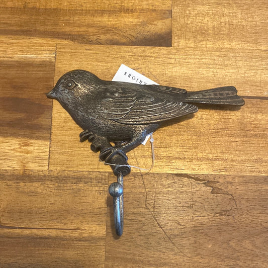 A pewter bird hook with a hook extended from its mouth, placed on a wooden surface.