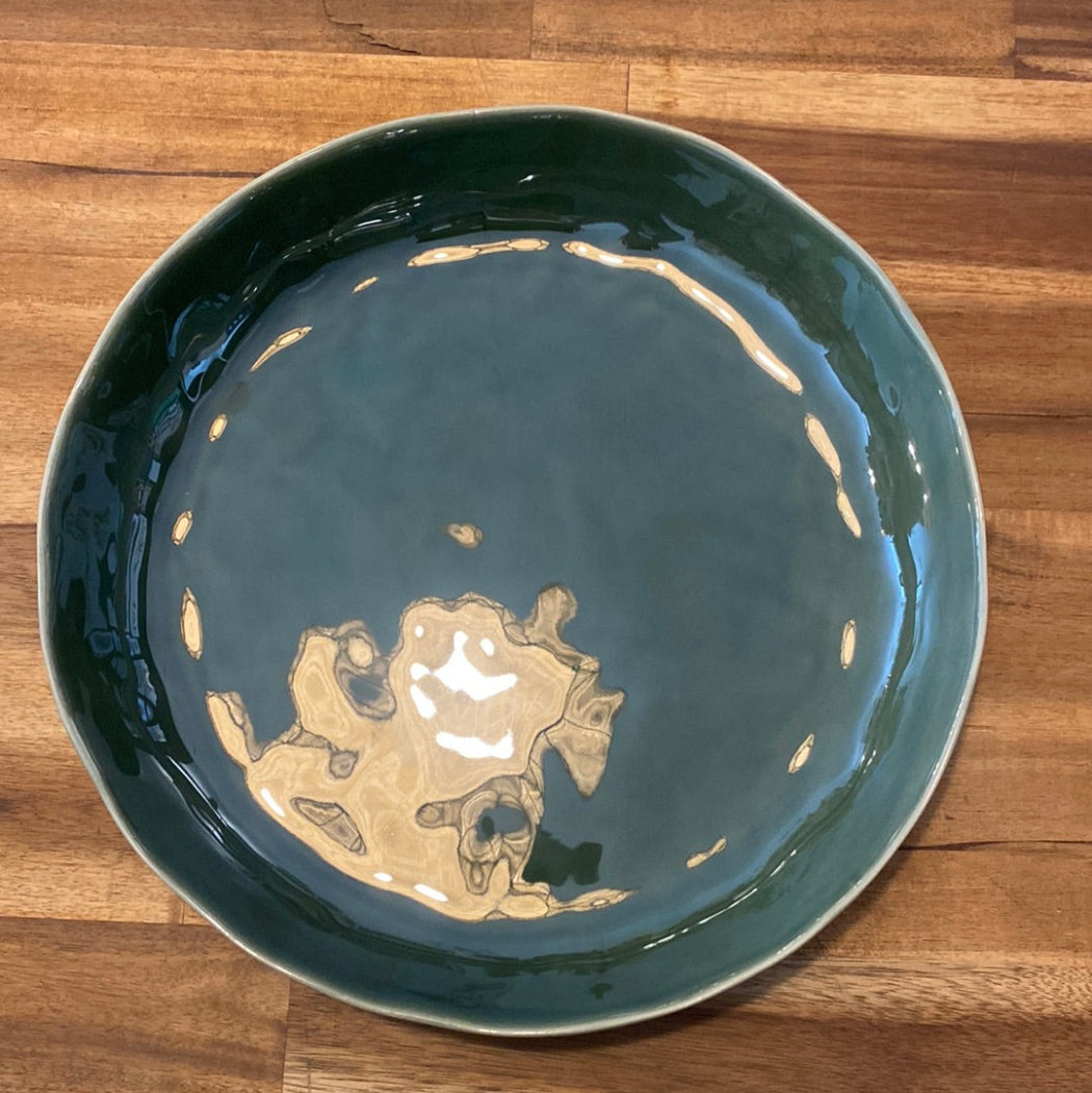 A round, green ceramic platter placed on a wooden surface.