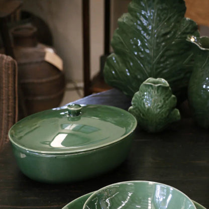 Green ceramic dish set on a wooden surface with decorative leaves.