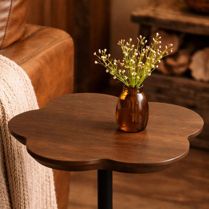 Wooden side table with a vase of flowers next to a brown leather sofa.