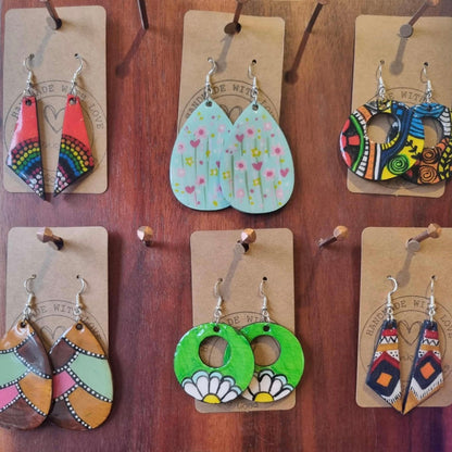 Collection of colorful earrings that have been handpainted on display with hanging cards on a wooden surface