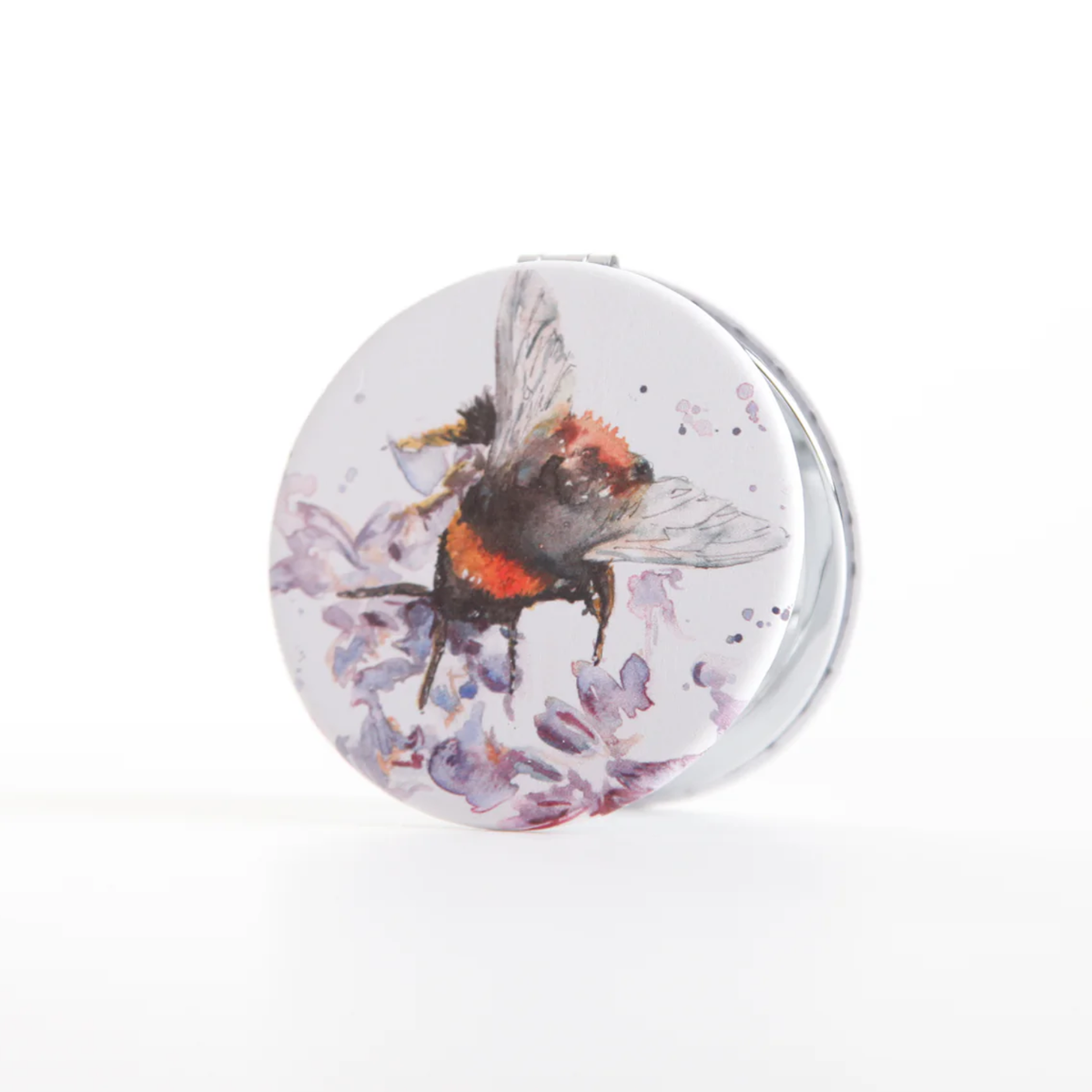 A round compact mirror featuring a watercolor illustration of a bumblebee on purple flowers, set against a clean white background.