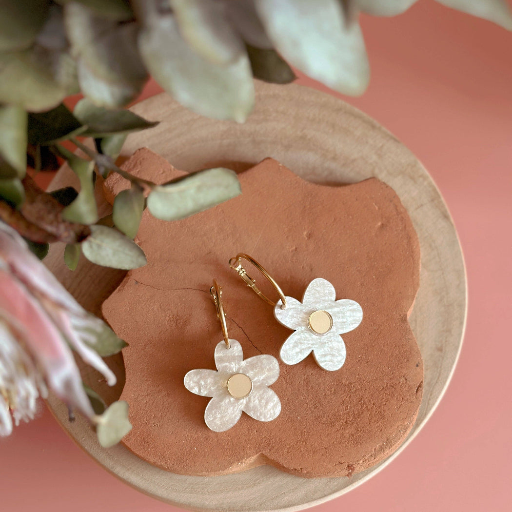 Flower-shaped earrings on a pink stone with greenery in the background