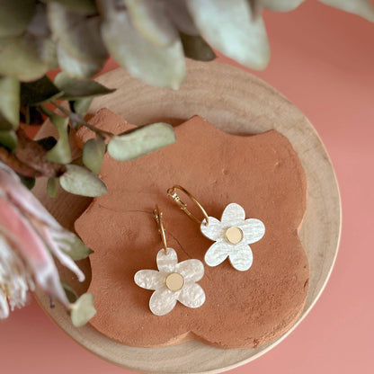 Flower-shaped earrings on a pink stone with greenery in the background
