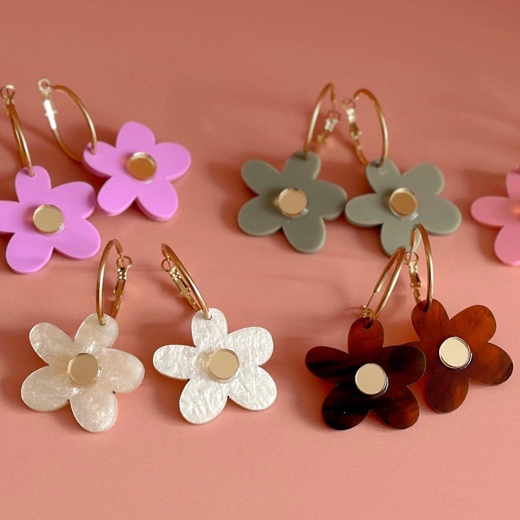 Set of colorful flower-shaped earrings on a pink background