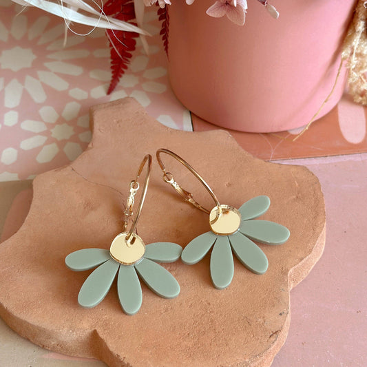 Green flower-shaped earrings on a wooden stand with a pink floral background