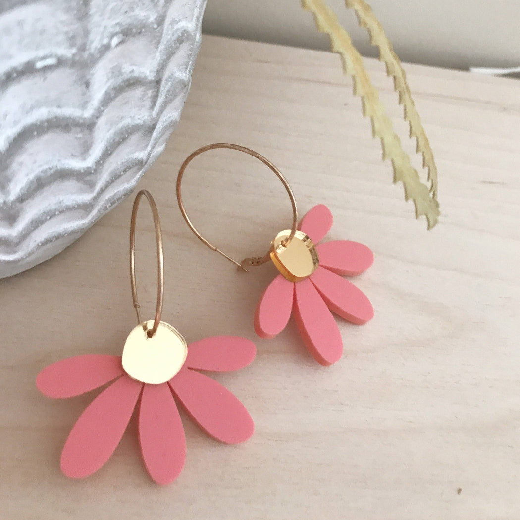 Pink flower-shaped earrings with gold centers on a light surface.