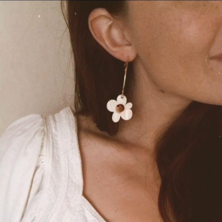 Woman wearing a white dress with floral earrings against a neutral background