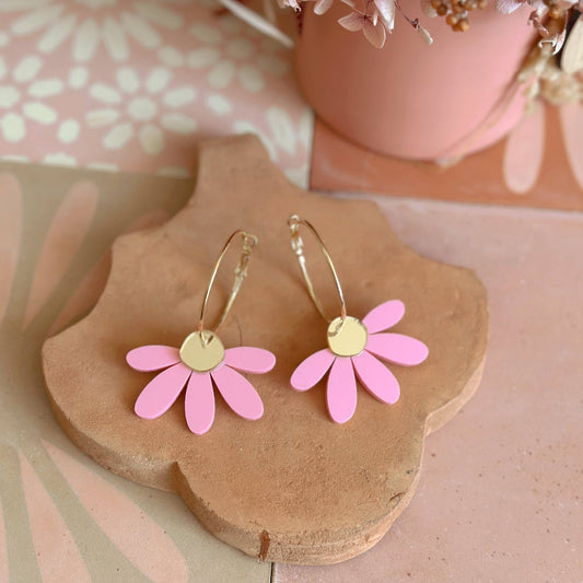 Pink flower-shaped earrings on a wooden stand with a floral background