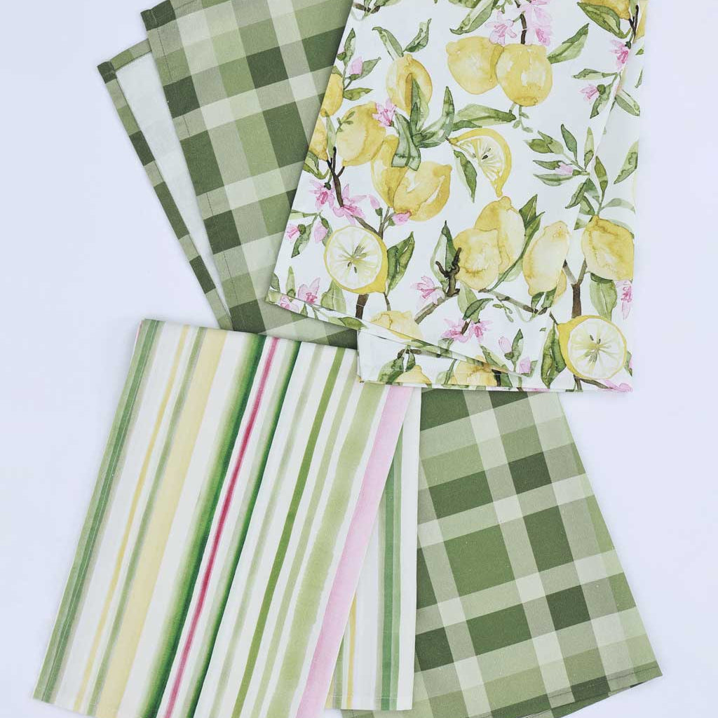 Set of 3 tea towels arranged on a white background, showing different patterns: two green plaid, one green-and-white striped with pink and yellow stripes, and one white with yellow lemons and pink flowers.