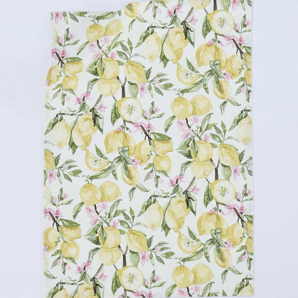 A rectangular kitchen towel or tea towel featuring a watercolor-style lemon and blossom print on a white background, photographed flat against a light gray studio backdrop.