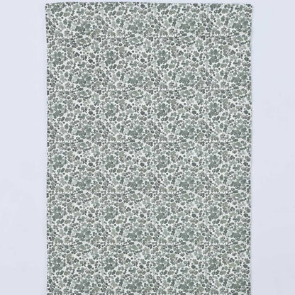 A rectangular fabric item, likely a tea towel or handkerchief, featuring a dense, small-scale floral and leaf pattern in muted sage green and gray on a white background, shown flat against a light gray backdrop.