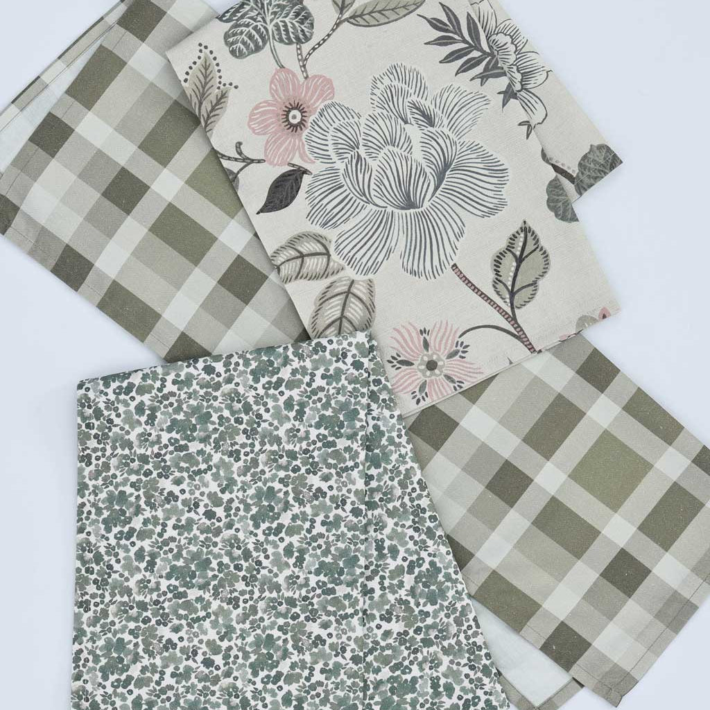 Three folded tea towels with different patterns displayed on a white background: a green and beige gingham, a cream floral print with pink flowers and green leaves, and a sage green and white floral print.