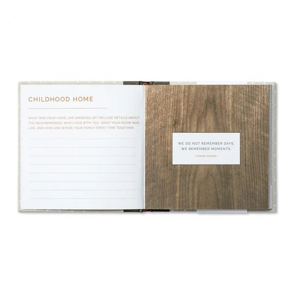 An open keepsake album or memory book with a white lined page titled 'CHILDHOOD HOME' on the left and a wood-grain cover insert with a small white label on the right, shown on a plain white background.