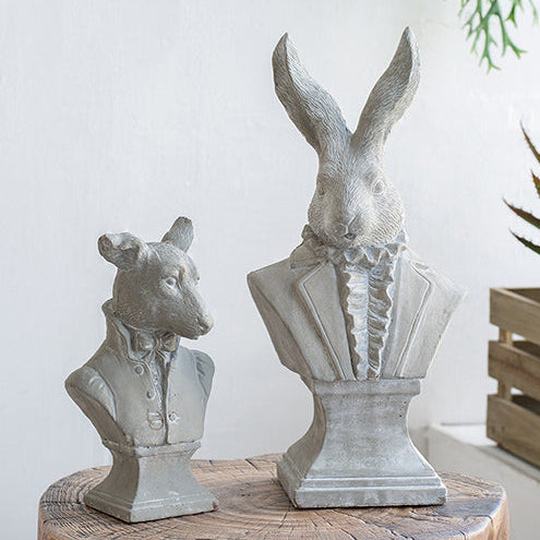 Decorative animal busts on a wooden stump with a white wall and plants in the background