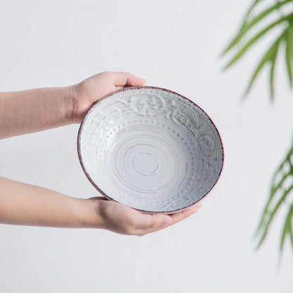 Person holding a textured ceramic bowl with a plant in the background