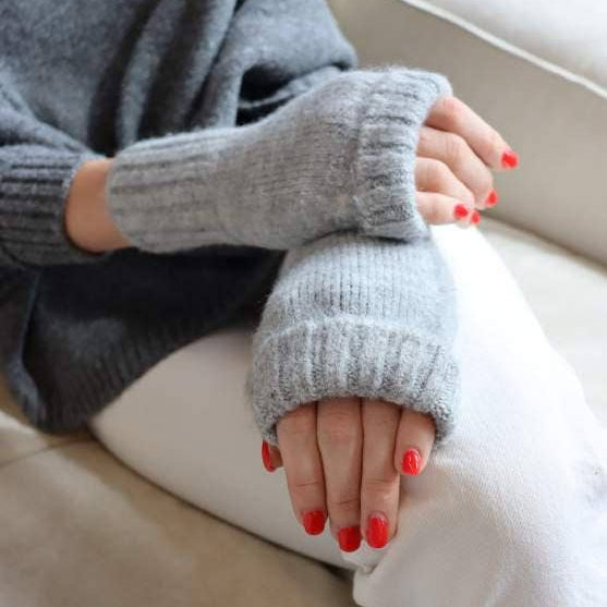 Person wearing a gray sweater and white pants with red nail polish sitting on a beige couch.