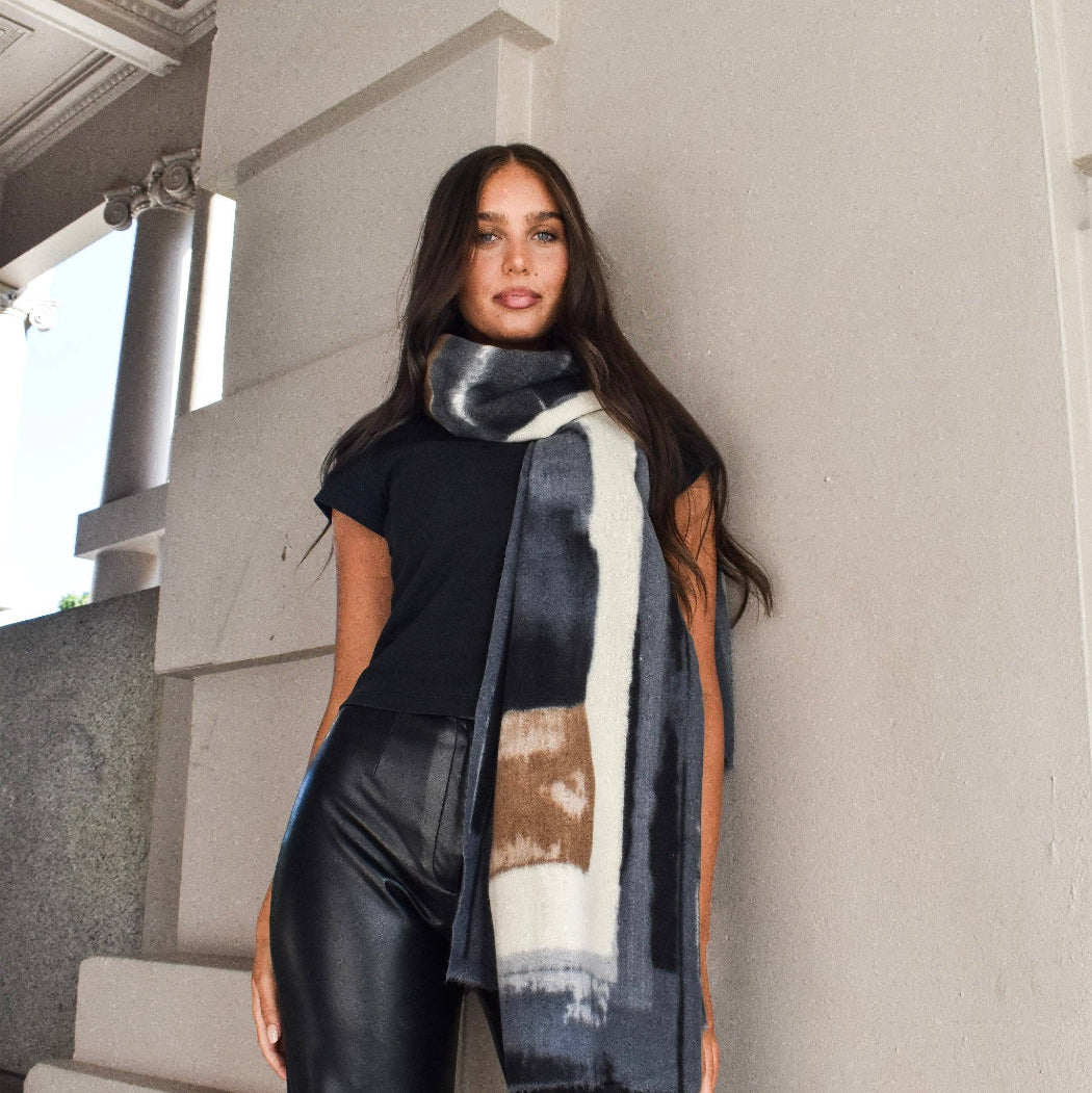 Woman wearing a patterned scarf standing against a light-colored wall.