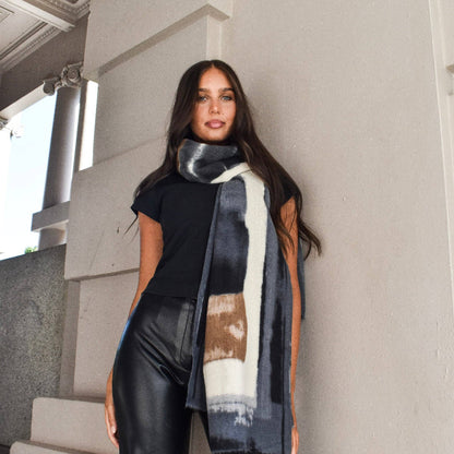 Woman wearing a patterned scarf standing against a light-colored wall.