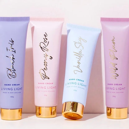 Four tubes of Living Light hand cream in different colors with gold caps, labeled with various scent names like Bling It, Peony Rose, Vanilla Sky, and Wild Plum.