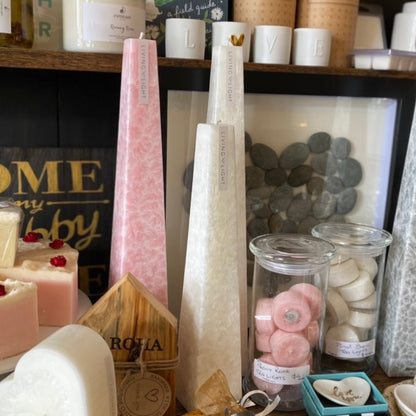 A selection of sculptural candles with a lace-like pattern, arranged vertically and displayed in a store setting with various other items.